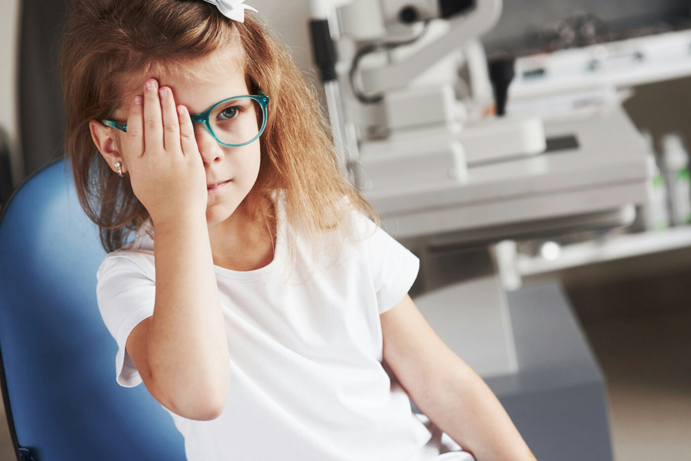 Young girl in glasses covering one eye during a pediatric vision test in front of an autorefractor at a children's eye exam with Dr. Roxanna Gangi in York Region