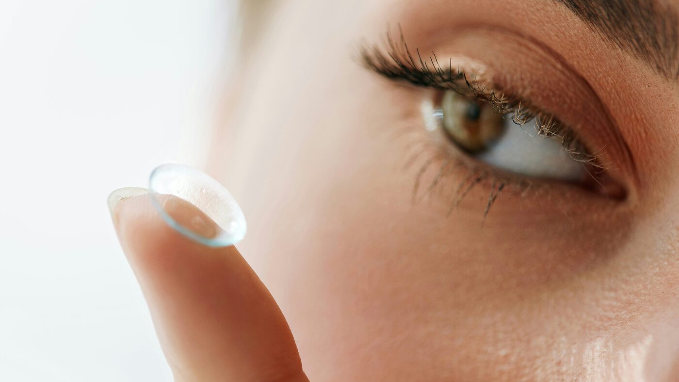 Close-up of a soft contact lens balanced on a fingertip beside a brown eye — contact lens options for myopia, hyperopia, and astigmatism with Dr. Roxanna Gangi at Pro Eye Exam in York Region