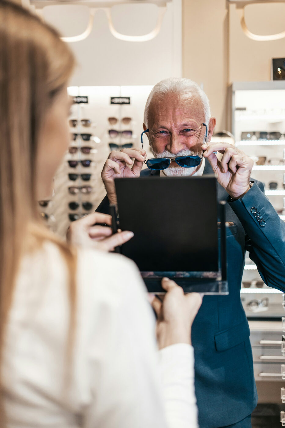 Senior man trying on prescription sunglasses while choosing eyewear with an optician during a senior eye care visit with Dr. Roxanna Gangi in York Region