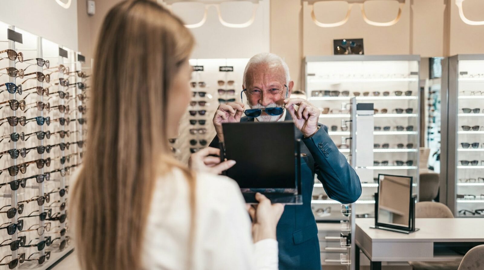 Senior man trying on prescription sunglasses while choosing eyewear with an optician during a senior eye care visit with Dr. Roxanna Gangi in York Region